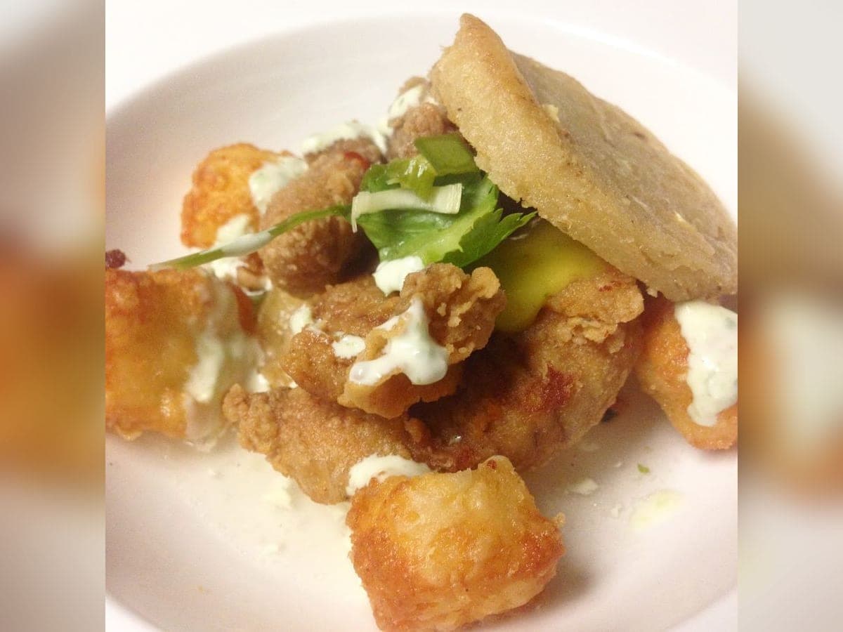 Arepa frita abierta en plato hondo con huevas fritas, queso y agüita de bagre