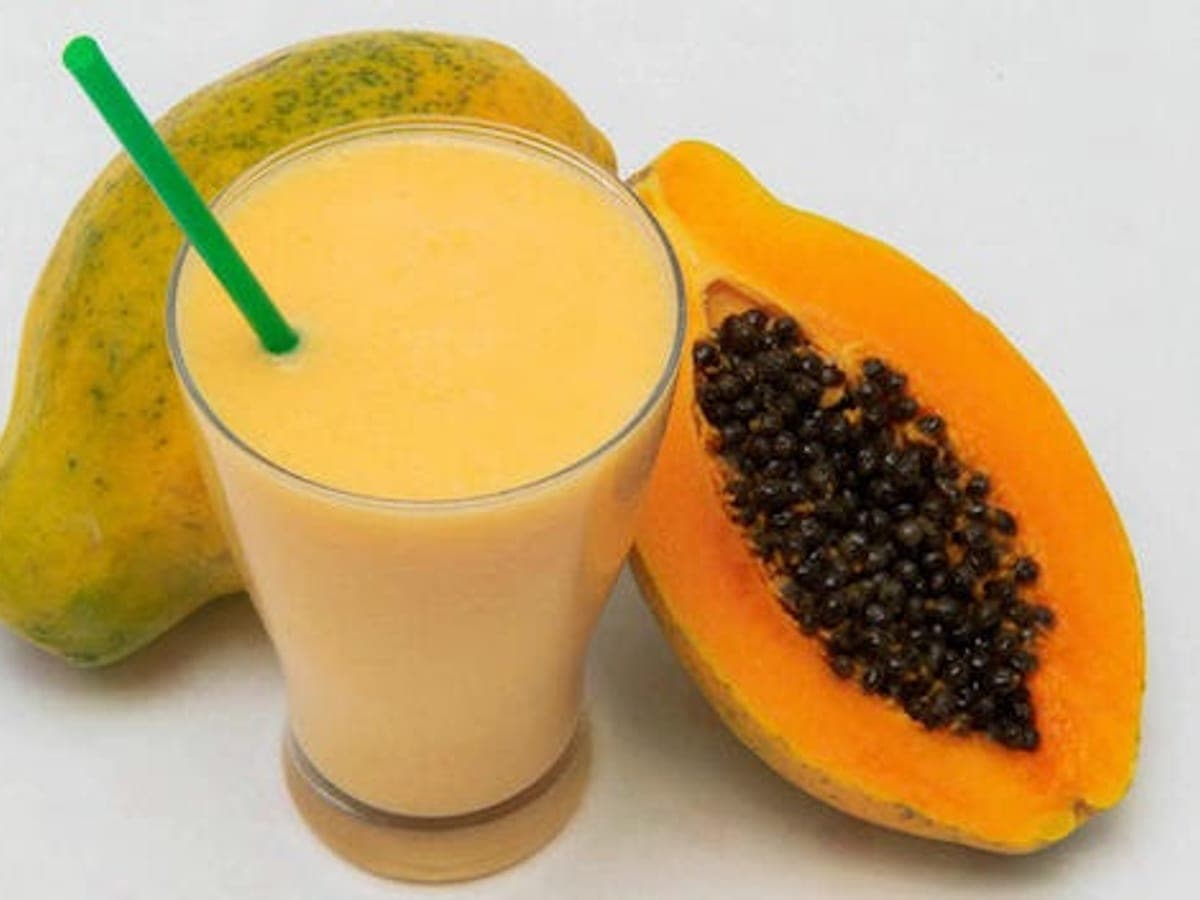 Vaso de batido de lechosa con una lechosa entera y otra abierta de fondo