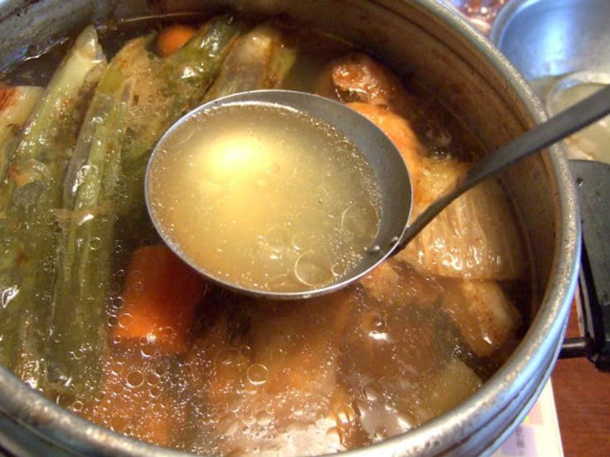 Caldo de pescado clarificado servido en un tazón, con espinas y verduras de fondo