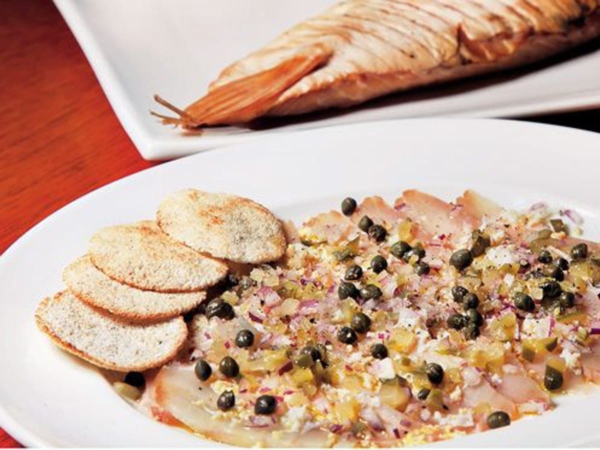Lonjas de carpaccio de lau lau ahumado con alcaparras, cebolla morada y cilantro
