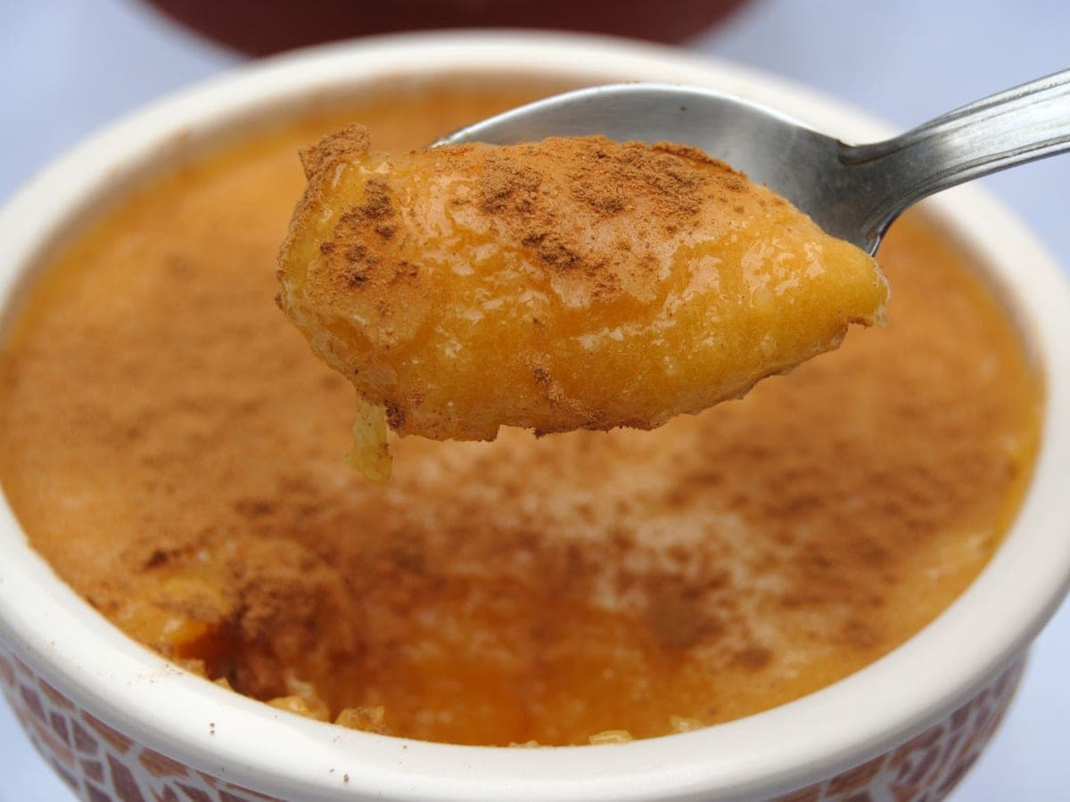 Cucharada de caspirotela espolvoreada con canela, sobre el postre servido en un pocillo