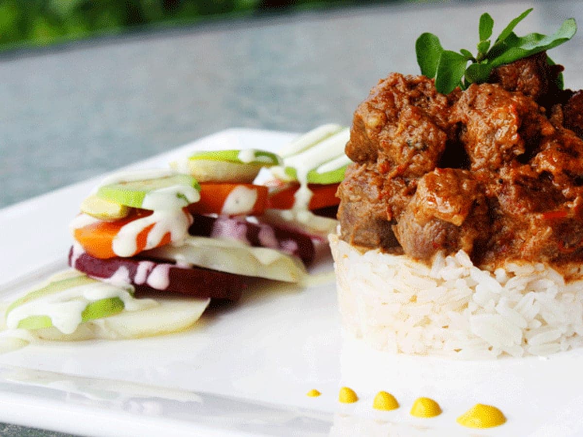 Chivo en coco guisado servido sobre arroz blanco, con ensalada de tomate, pepino y cebolla