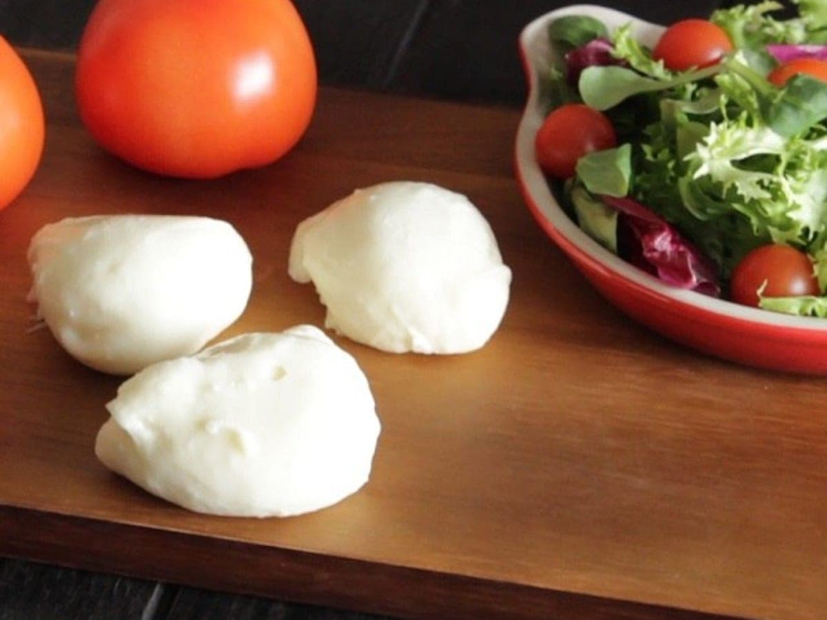 Bolas de mozzarella vegana sobre una tabla de madera, junto a tomates y ensalada