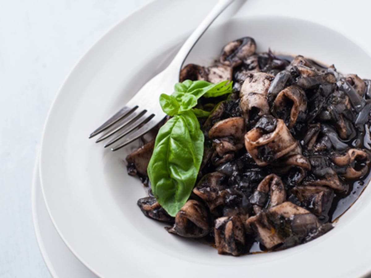Plato de espagueti negro con rodajas de calamar y dados de tomate seco