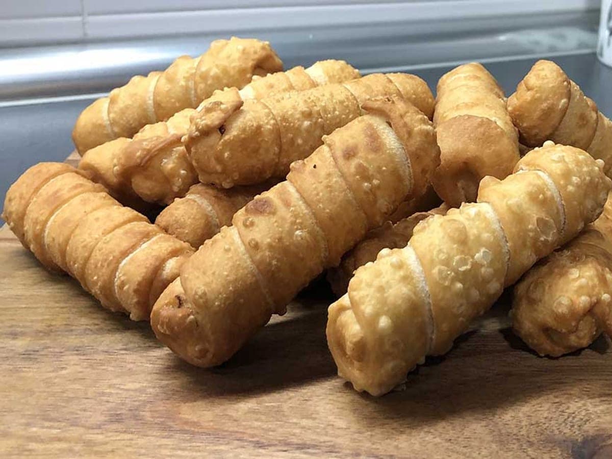 Tequeños fritos y dorados, apilados en un plato, con el queso asomando