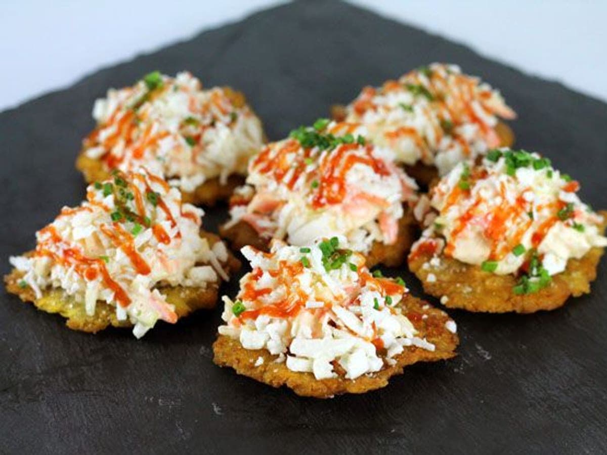 Tostones de plátano verde cubiertos de ensalada rallada, queso blanco y salsas